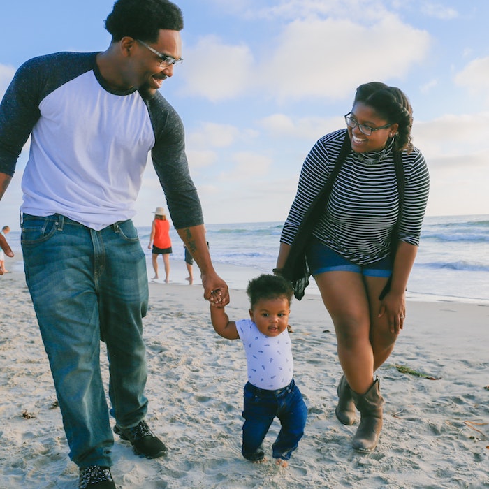 Image of a couple smiling while walking a baby between them on the beach.