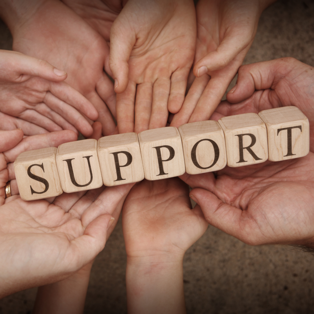 Multiple hands surrounding wooden blocks that spell out the word "support".