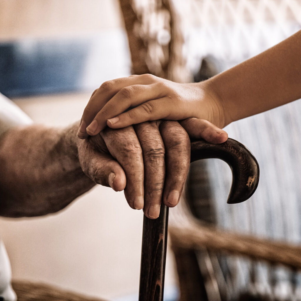 Image of a child's hand over an old man's hand holding a cane for Jewish Healing Services.